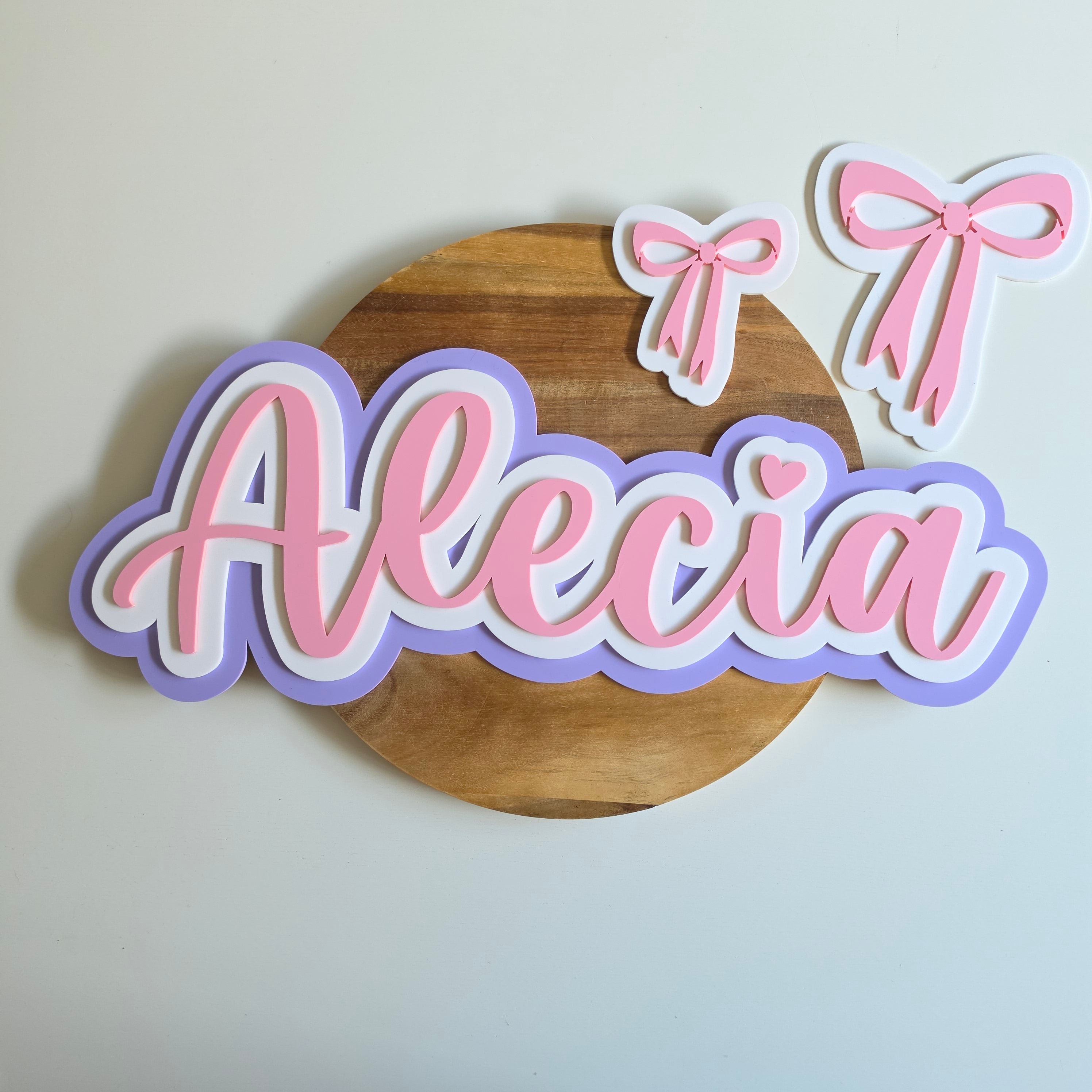 Wooden round sign with 'Alecia' in pink and purple on a white background